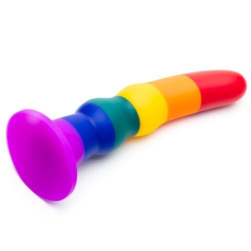 An angled view of the True Colors rainbow dildo on its side on a white surface, showing the suction-cup base.
