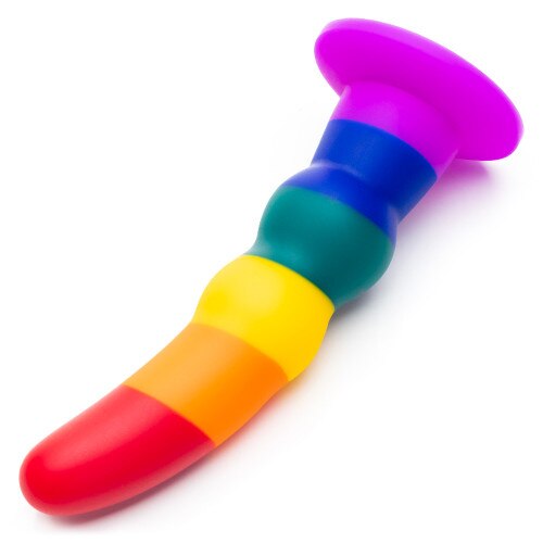 An angled view of the rainbow True Colors dildo on its side on a white surface, highlighting the undulating shape of the shaft.