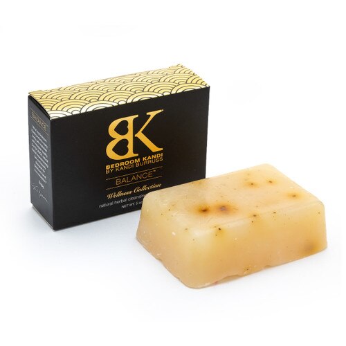 An image of the herbal cleaning Balance Bar with its black and gold box on a white background. The soap is rectangular and yellow with natural dark speckles and irregularities.