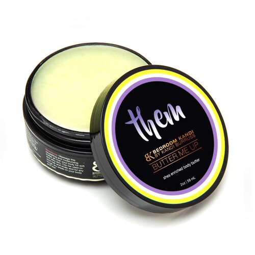 An image of a round container of Butter Me Up in the Them scent. The container is open with the lid propped up in front of it, revealing the smooth pale yellow surface of the body butter.