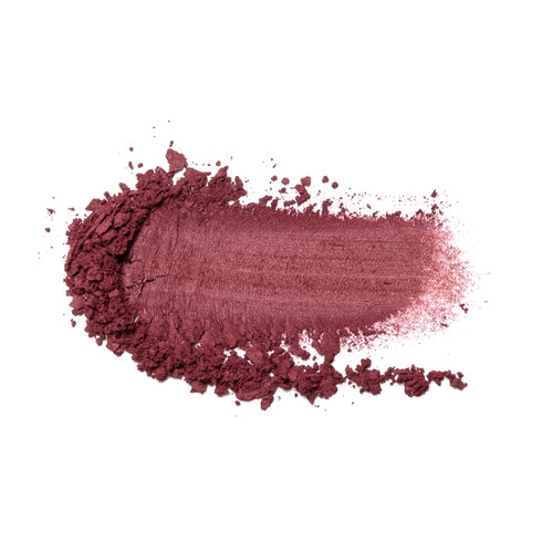 A smudge of crumbled powder blush on a white surface. The color is “Bashful”, a rich warm plum.