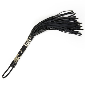 An overhead image of the Command Desire flogger on a white background. The flogger has a filigree-patterned handle and numerous thin leather tails.