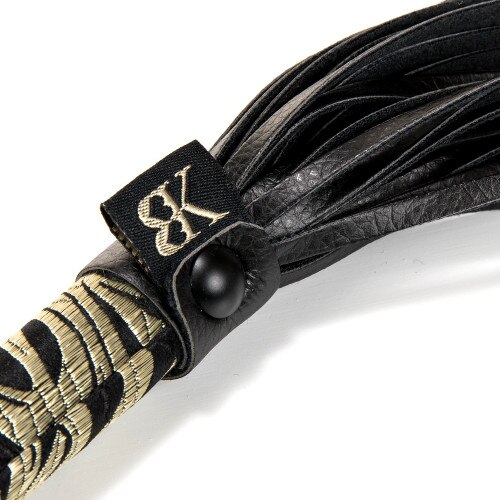 A close up of the flogger that shows the embroidered texture of the filigree on the handle and the supple texture of the leather tails.
