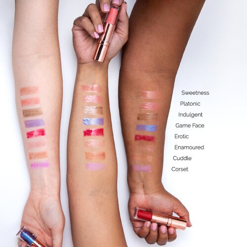 An image of three outstretched arms of differing skin tones showcasing different colors of Glaze lip glosses in swatches on each arm for comparison. Each hand clasps a different tube.