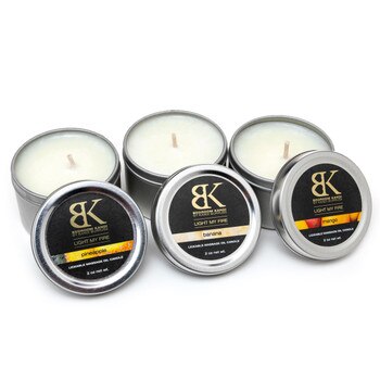 An image of three small flavored massage oil candle tins in a row with their lids propped up in front of them, displaying the flavors.