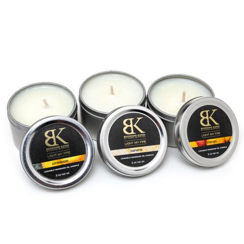 An image of three small flavored massage oil candle tins in a row with their lids propped up in front of them, displaying the flavors.