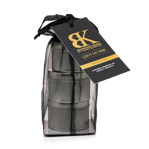 An image of three small massage oil candle tins stacked on top of each other in a black organza bag. A tag attached to the bag reads "Light My Fire" and Assorted Flavors..