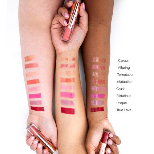 An image of three outstretched arms of differing skin tones showcasing different colors of liquid satin lip shine in swatches on each arm for comparison. Each hand clasps a different tube.