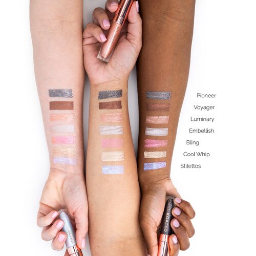 An image of three outstretched arms of differing skin tones showcasing different colors of Luster liquid metal eyeshadows in swatches on each arm for comparison. Each hand clasps a different tube.