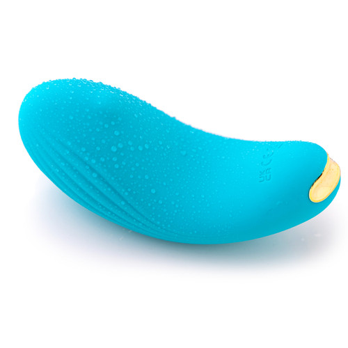 A view of the turquoise Ripple massager on its side on a white background covered in water droplets. The massage is waterproof.