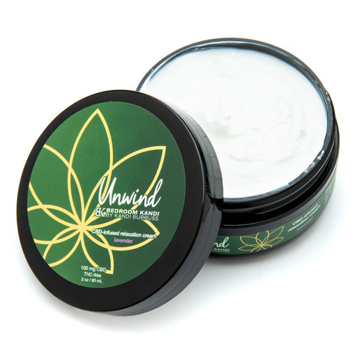 An open two ounce black round jar of Unwind CBD-infused relaxation cream. The label is green and gold over a black jar on a white background. The thick white cream is visible inside the jar.