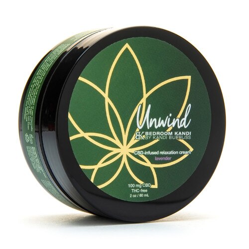 A closed jar of 2 ounce Unwind CBD-infused relaxation cream on its side. The label is green and gold on a black round jar.