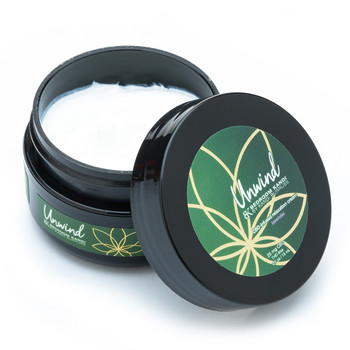 An open half ounce black round jar of Unwind CBD-infused relaxation cream. The label is green and gold over a black jar on a white background. The thick white cream is visible inside the jar.