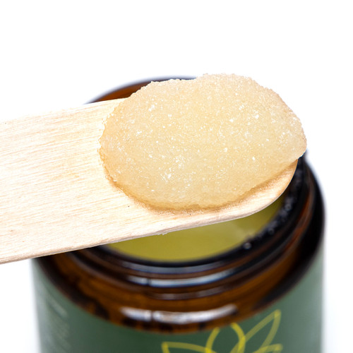 A close up of the moisturizing salt scrub on a wooden applicator held above the jar.