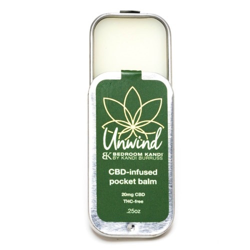 A partially-open tin of Unwind Pocket Balm, revealing the white balm within and the sliding closure of the travel-friendly tin