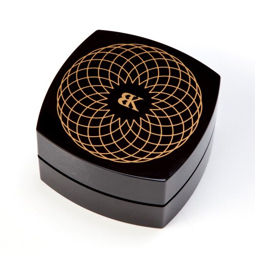 An image of the closed Make Me Over compact charging case. It is made of black plastic with an elegant gold pattern on the top with the BK logo.